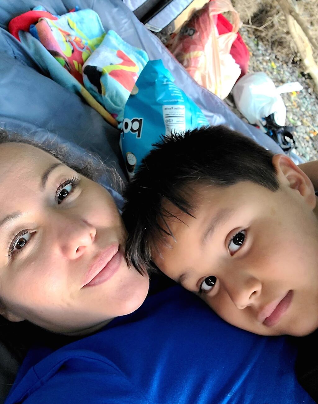 A woman and her young son cuddling on a blanket.